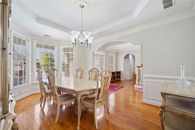 dining room with visible vents, light wood-style floors, an inviting chandelier, arched walkways, and a raised ceiling