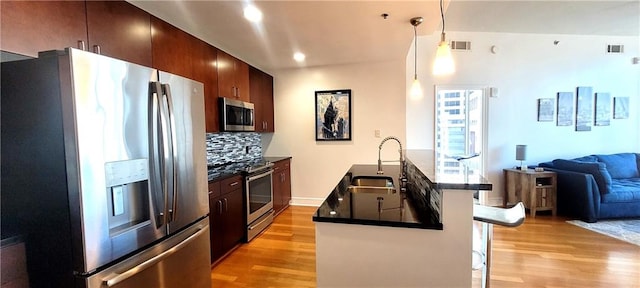 kitchen with sink, stainless steel appliances, a kitchen breakfast bar, decorative light fixtures, and light wood-type flooring