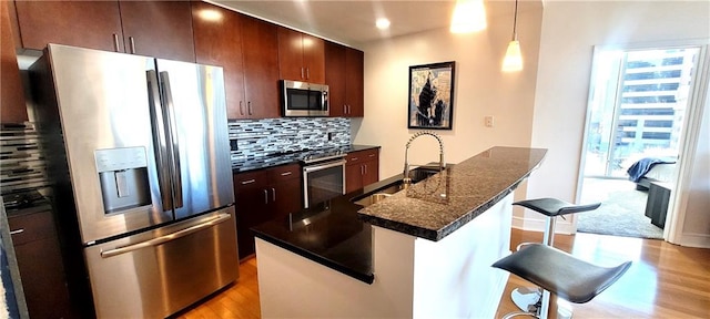 kitchen featuring a center island with sink, a breakfast bar area, appliances with stainless steel finishes, a sink, and dark stone countertops