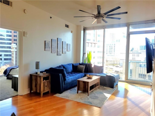 living room featuring expansive windows, visible vents, ceiling fan, and wood finished floors