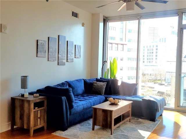 living area featuring expansive windows, ceiling fan, wood finished floors, and visible vents