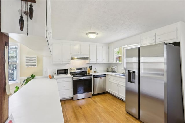 kitchen with light wood finished floors, under cabinet range hood, light countertops, stainless steel appliances, and white cabinetry