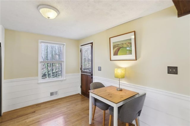 dining room featuring a wainscoted wall, light wood-style floors, visible vents, and a textured ceiling