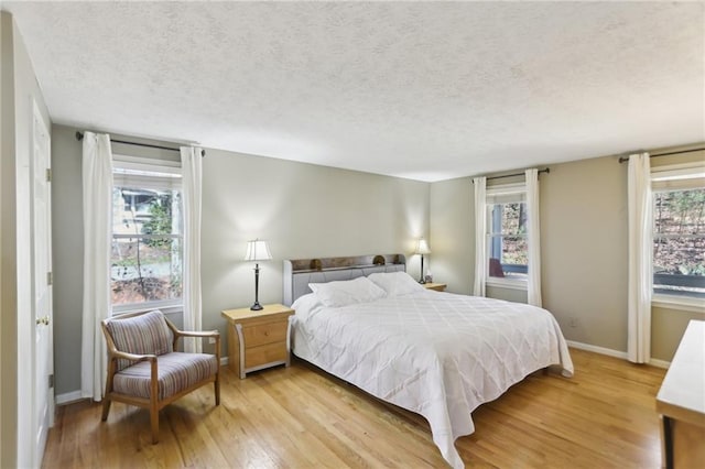 bedroom featuring baseboards, light wood finished floors, and a textured ceiling