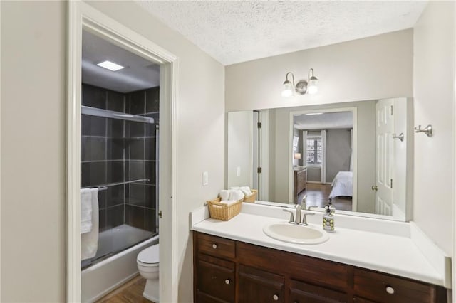 bathroom with toilet, ensuite bathroom, a textured ceiling, combined bath / shower with glass door, and vanity