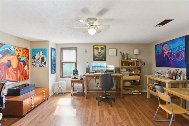 office area featuring wood finished floors, baseboards, visible vents, ceiling fan, and a textured ceiling