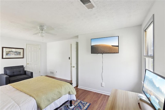 bedroom with visible vents, baseboards, a textured ceiling, and wood finished floors