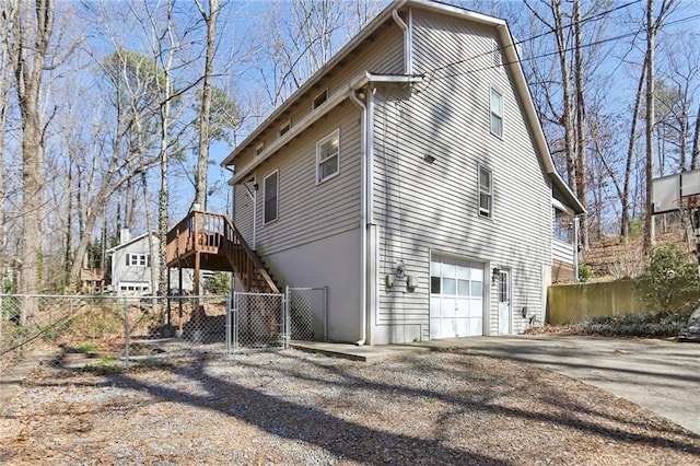 view of side of property featuring a gate, fence, driveway, an attached garage, and stairs