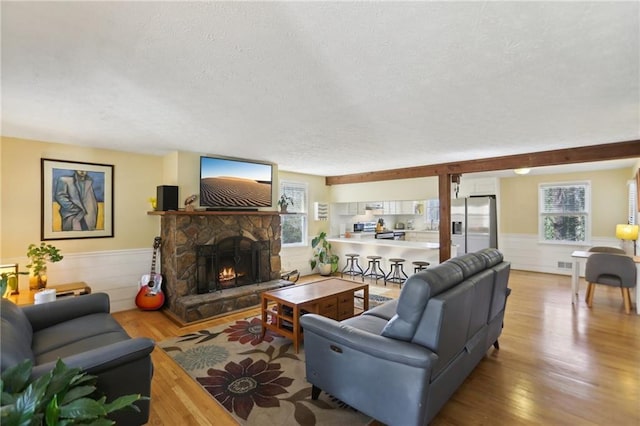 living area featuring wainscoting, a fireplace, a textured ceiling, and wood finished floors