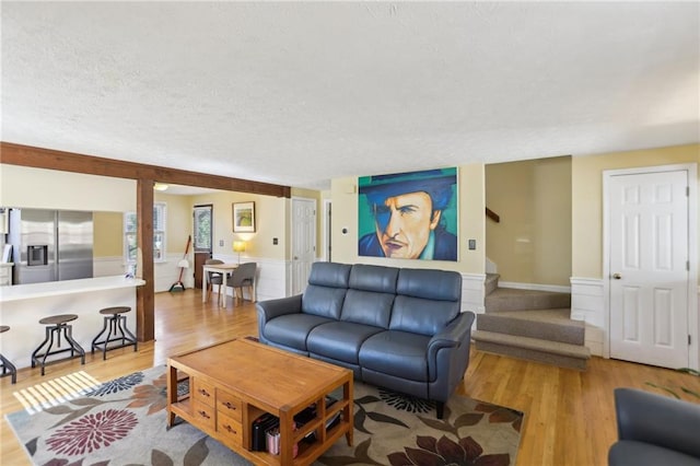 living room featuring wainscoting, a textured ceiling, wood finished floors, and stairs