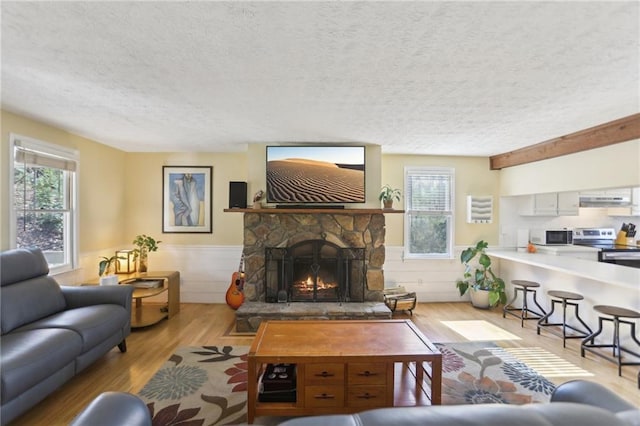 living room with a stone fireplace, wood finished floors, a healthy amount of sunlight, and wainscoting