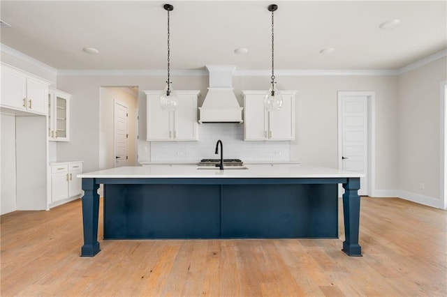 kitchen with custom exhaust hood, a kitchen island with sink, white cabinets, and hanging light fixtures