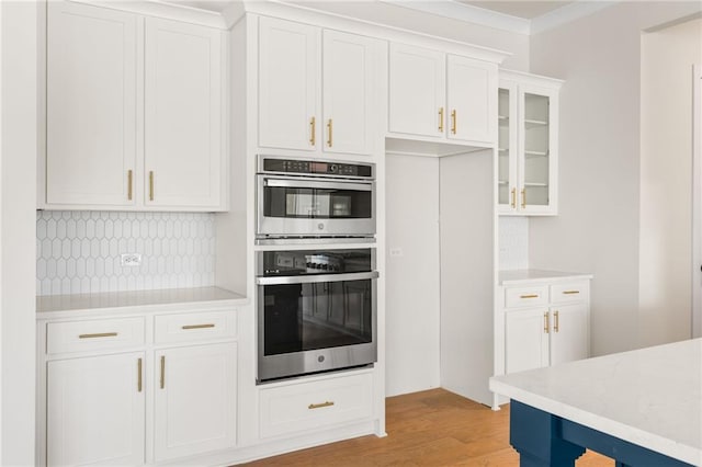 kitchen featuring light hardwood / wood-style flooring, tasteful backsplash, double oven, ornamental molding, and white cabinetry