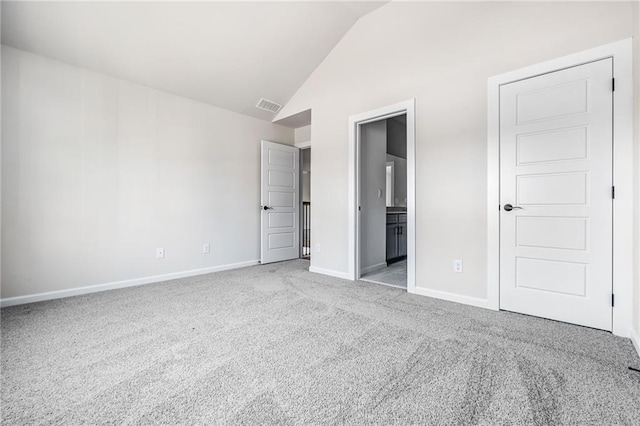 unfurnished bedroom featuring light carpet, vaulted ceiling, and ensuite bath