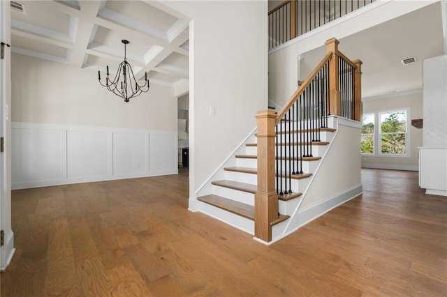 stairs with beam ceiling, a notable chandelier, crown molding, coffered ceiling, and hardwood / wood-style floors