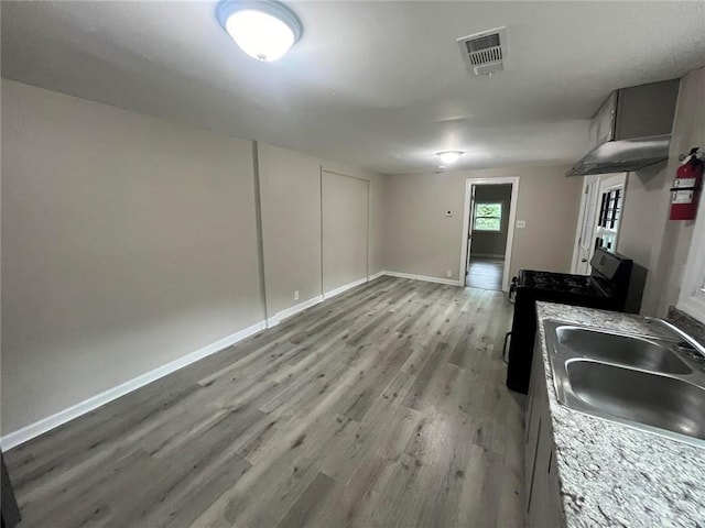 kitchen featuring gray cabinets, light wood-type flooring, black range with gas cooktop, light stone counters, and sink