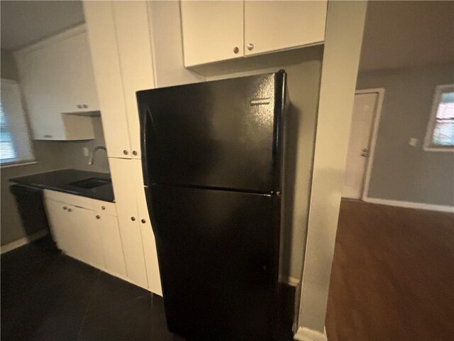 kitchen featuring black fridge, white cabinetry, and sink