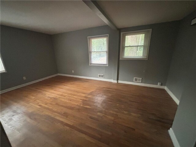 empty room with beamed ceiling and dark wood-type flooring