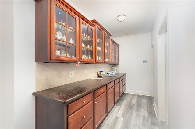 bar with tasteful backsplash, dark stone countertops, and light hardwood / wood-style flooring