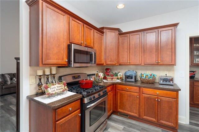 kitchen with appliances with stainless steel finishes, light hardwood / wood-style floors, and tasteful backsplash