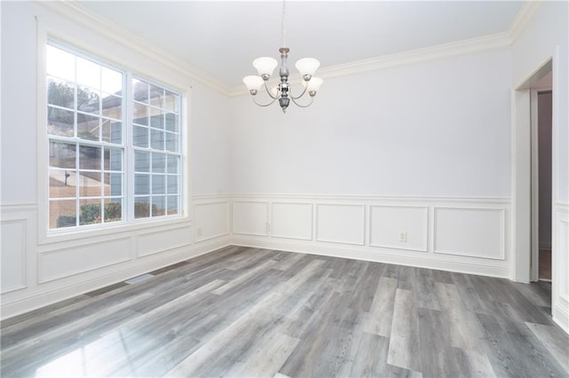 empty room featuring hardwood / wood-style floors, ornamental molding, and an inviting chandelier