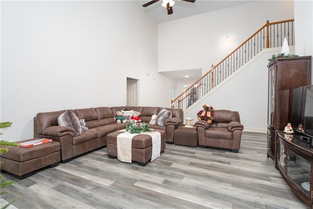 living room with ceiling fan, light wood-type flooring, and a towering ceiling