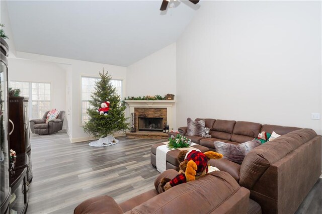 living room with high vaulted ceiling, light hardwood / wood-style flooring, a stone fireplace, and ceiling fan