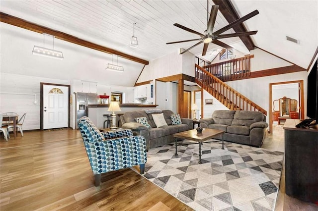 living room with ceiling fan, beamed ceiling, light wood finished floors, stairway, and high vaulted ceiling