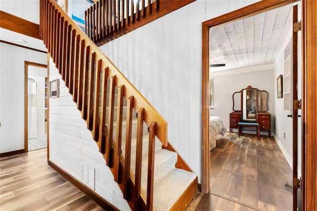 staircase featuring wood walls, baseboards, crown molding, and wood finished floors