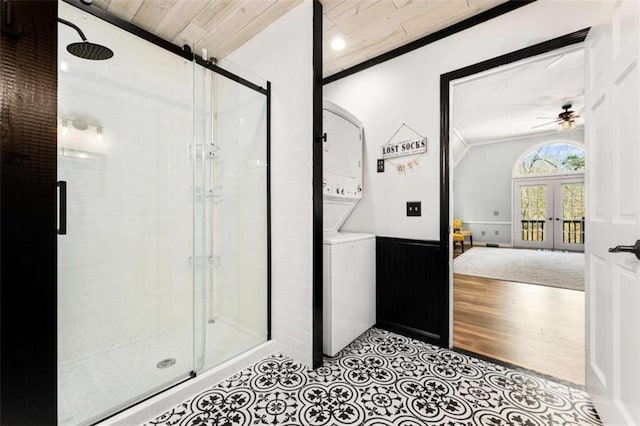 bathroom featuring a stall shower, a ceiling fan, a wainscoted wall, stacked washing maching and dryer, and french doors