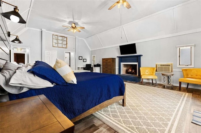 bedroom with a wall mounted AC, vaulted ceiling, a brick fireplace, ceiling fan, and wood finished floors