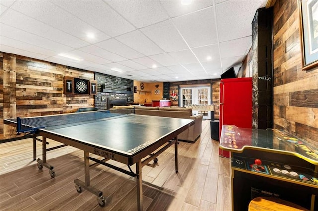 game room with wood walls, a paneled ceiling, wood finished floors, and a fireplace