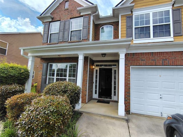view of exterior entry with brick siding, a garage, and a porch