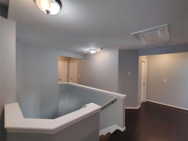 corridor featuring baseboards, attic access, dark wood-style floors, and an upstairs landing