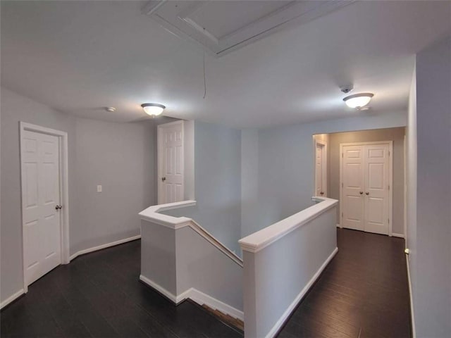 hallway with dark wood-style flooring, baseboards, and an upstairs landing