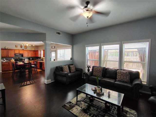 living room with ornate columns, a ceiling fan, visible vents, and dark wood finished floors