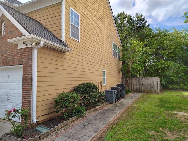 view of property exterior with fence, roof with shingles, central AC, a garage, and a lawn
