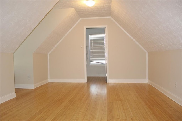 bonus room with a textured ceiling, light hardwood / wood-style floors, and vaulted ceiling