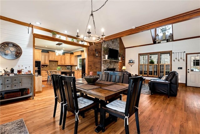 dining area featuring light wood-style flooring, an inviting chandelier, vaulted ceiling, and a fireplace