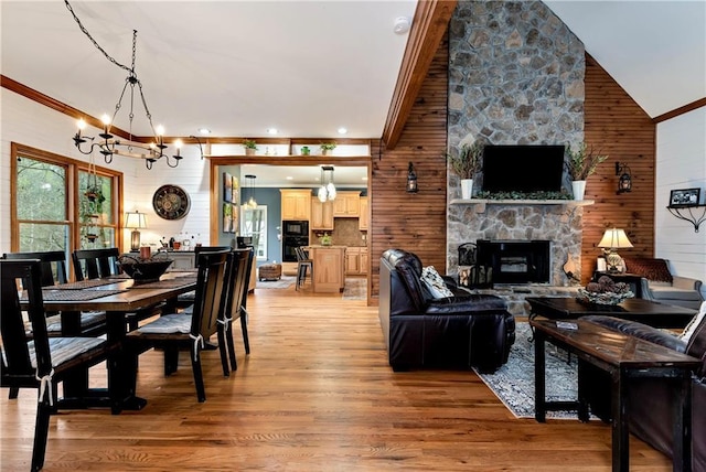 dining space with a stone fireplace, a chandelier, a towering ceiling, wood walls, and light wood-style flooring