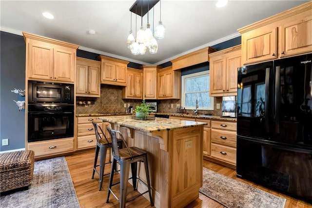kitchen with a center island, light brown cabinets, light wood finished floors, black appliances, and light stone countertops