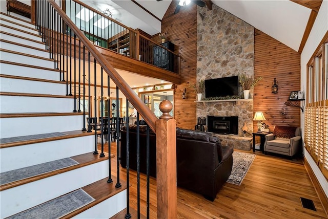 stairway featuring visible vents, a stone fireplace, a ceiling fan, wood finished floors, and wood walls