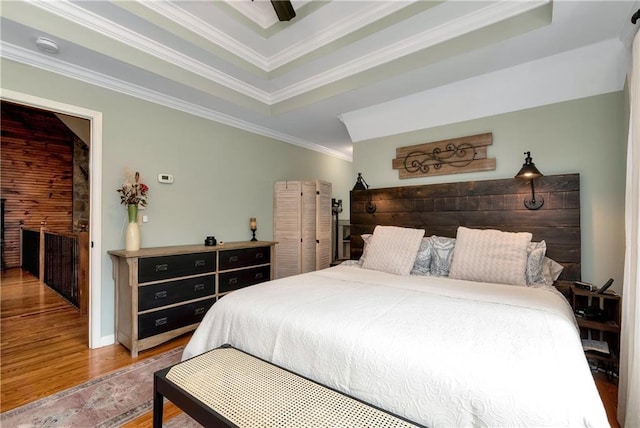 bedroom with a raised ceiling, wood finished floors, ceiling fan, and ornamental molding