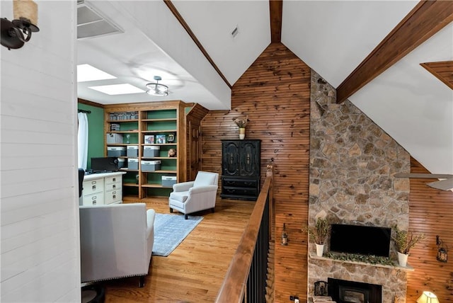 living room featuring a fireplace, wooden walls, beam ceiling, high vaulted ceiling, and wood finished floors