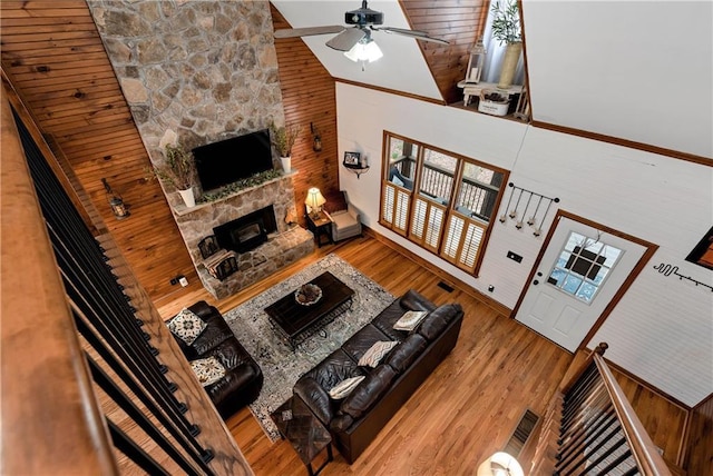 living area with a stone fireplace, high vaulted ceiling, ceiling fan, and wood finished floors