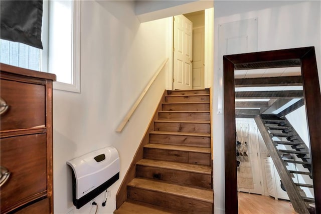staircase with wood finished floors, beam ceiling, and heating unit