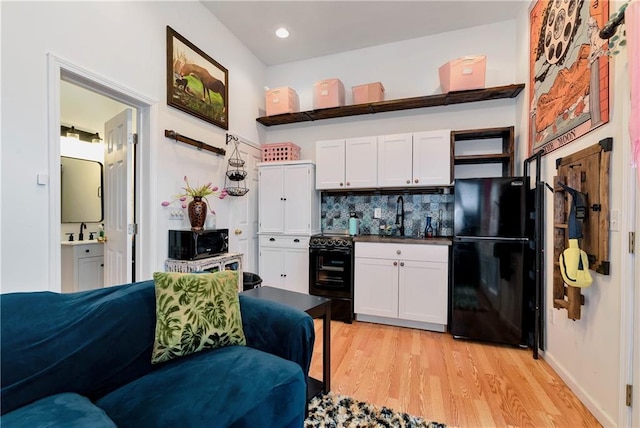 kitchen featuring white cabinets, dark countertops, light wood-style floors, black appliances, and decorative backsplash