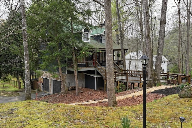 back of house featuring a wooden deck, stairway, stone siding, a garage, and driveway