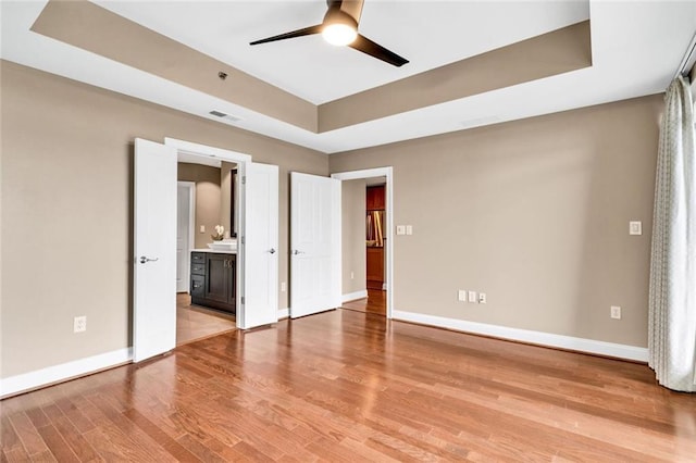 2881 Peachtree Rd NE Unit 1202, Atlanta, GA 30305 - unfurnished bedroom with a tray ceiling, light wood finished floors, baseboards, ensuite bathroom, and a ceiling fan