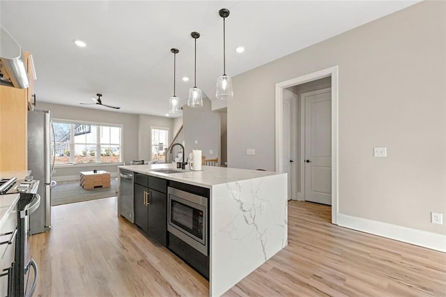 kitchen featuring pendant lighting, sink, appliances with stainless steel finishes, light stone counters, and a center island with sink